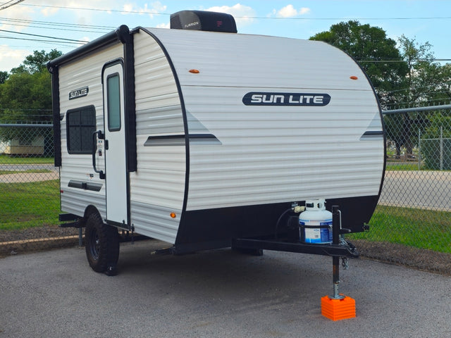 Compact white "SUN LITE" travel trailer rv rental with awning, propane tank, and rugged tires, parked on asphalt.