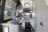Spacious RV rental interior featuring a modern kitchenette, lounge seating, and large windows for comfortable mobile living.