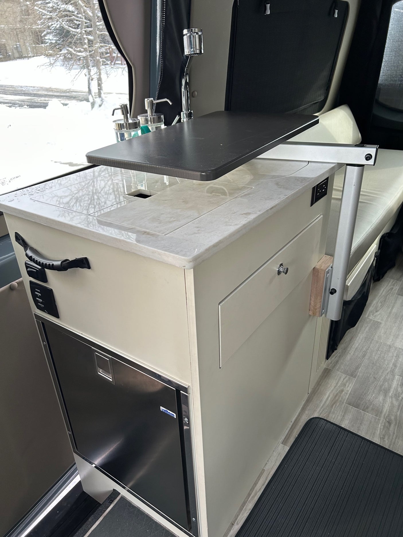 RV rental: View of a modern camper van interior, highlighting a compact kitchen with sink, pull-out table, and fridge.