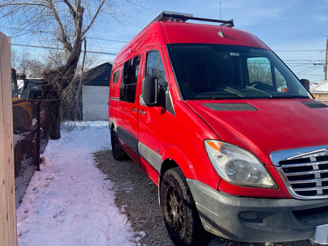 Bright red RV rental parked in winter, showcasing roof-mounted solar panels. Ideal for your next camper van adventure.