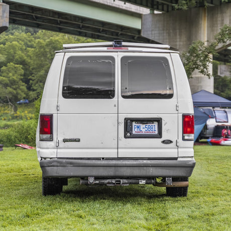 Rear view of a white Ford van (NC plate PML-5881) on grass under a bridge. Great for an RV rental or camping adventure.