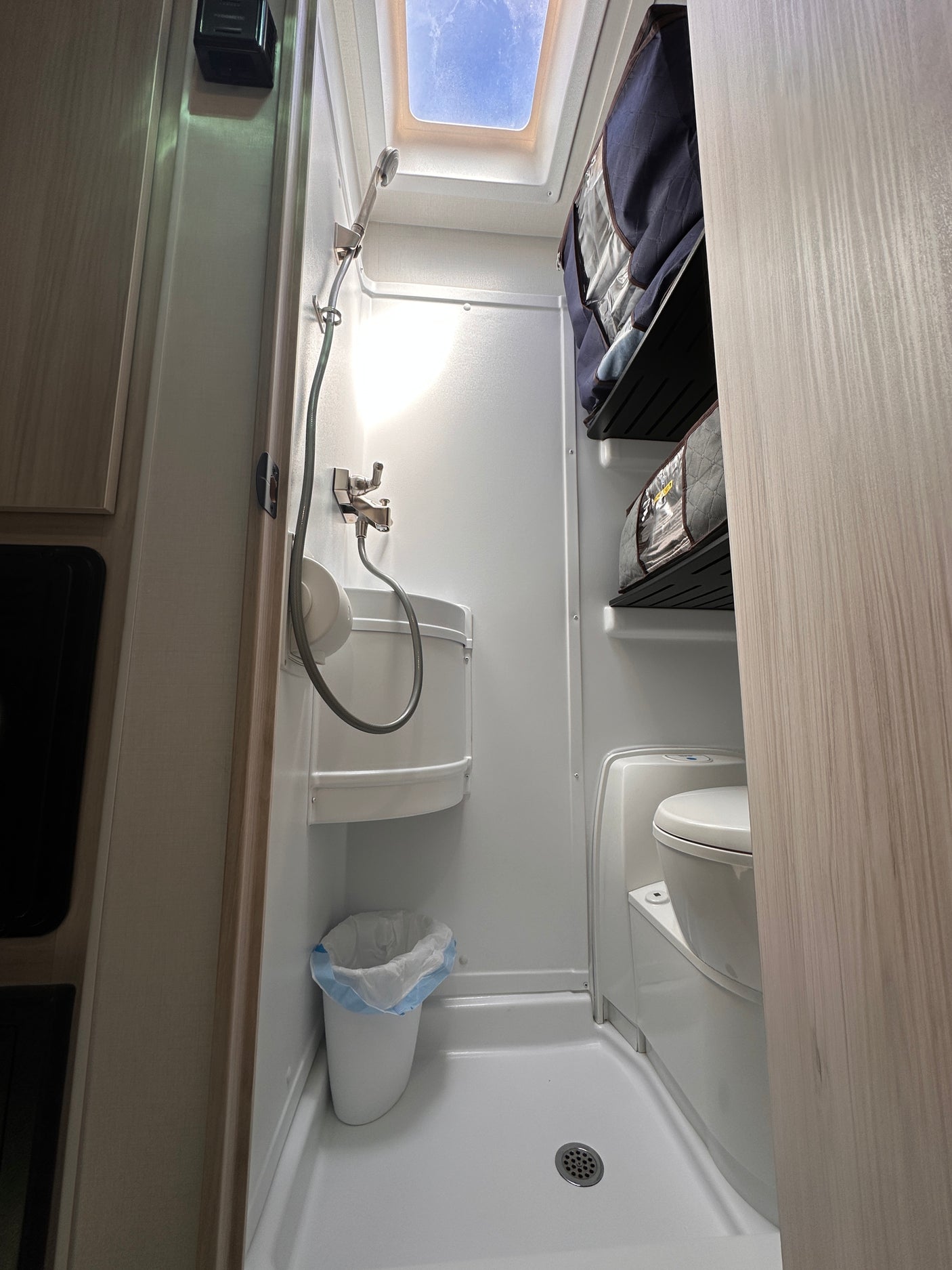 Compact RV rental wet bath with shower, toilet, sink, trash, and storage. Skylight visible.