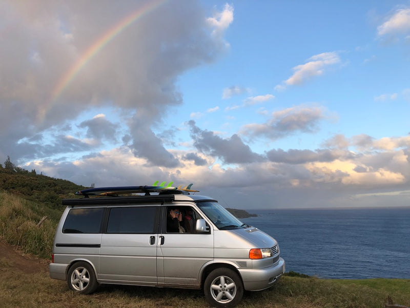 A silver rv rental camper van, equipped with surfboards, overlooks the ocean from a grassy cliff under a vivid rainbow. Van life adventure! — photo 3