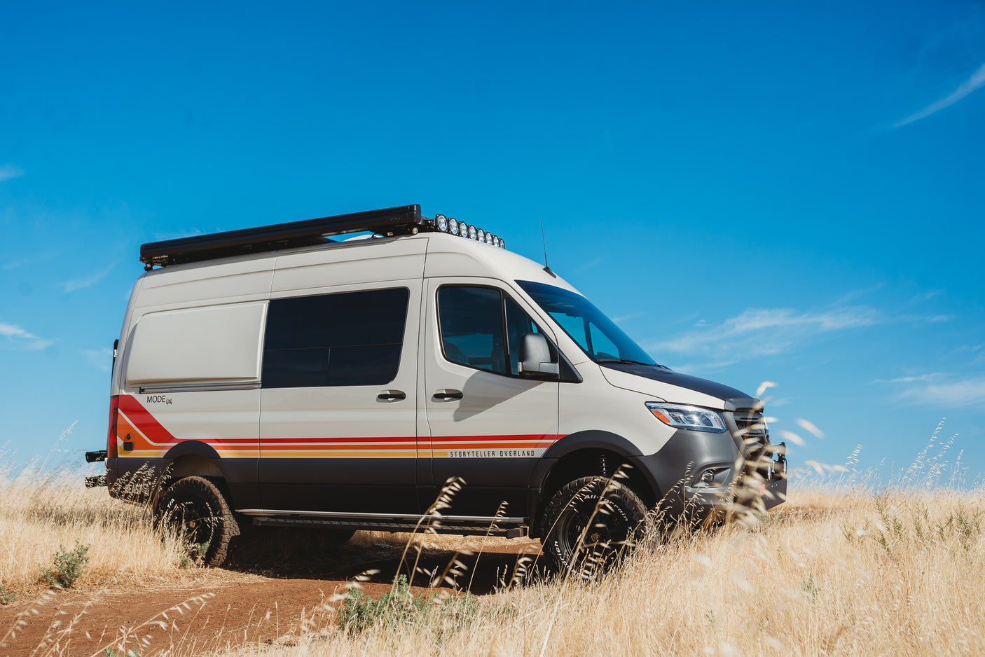 Off-road Storyteller Overland camper van, a great RV rental for adventure. White van with stripes in a golden field.
