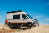 Off-road Storyteller Overland camper van, a great RV rental for adventure. White van with stripes in a golden field.
