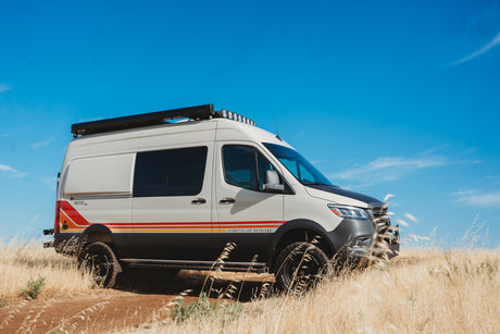 Off-road Storyteller Overland camper van, a great RV rental for adventure. White van with stripes in a golden field.