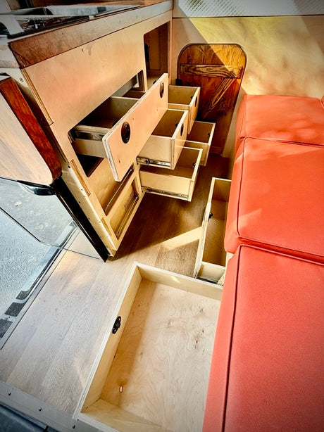 RV rental with efficient wood storage drawers pulled out, an orange bench seat, and light wood flooring in a compact camper.