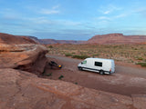 Enjoying the desert! A white RV rental van is set up with a campfire, chairs, and stunning red rock views.