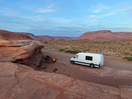 Enjoying the desert! A white RV rental van is set up with a campfire, chairs, and stunning red rock views.