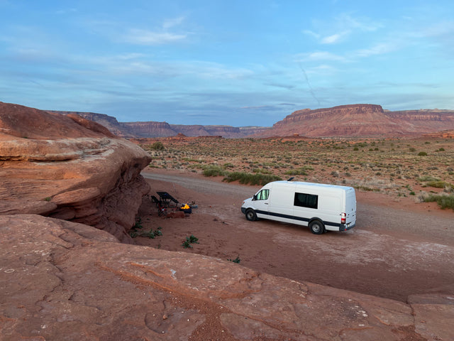 Enjoying the desert! A white RV rental van is set up with a campfire, chairs, and stunning red rock views.