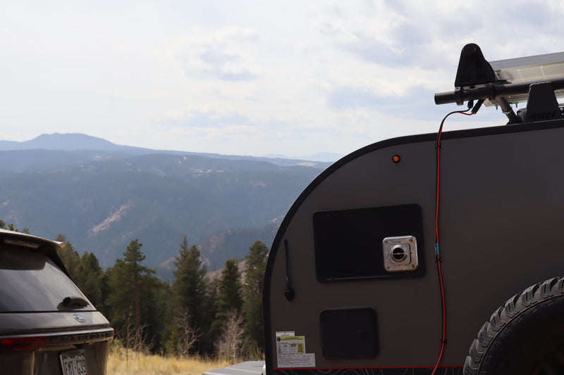 A gray RV rental teardrop trailer, equipped with a solar panel, and an SUV overlooking a vast mountain range. — photo 6