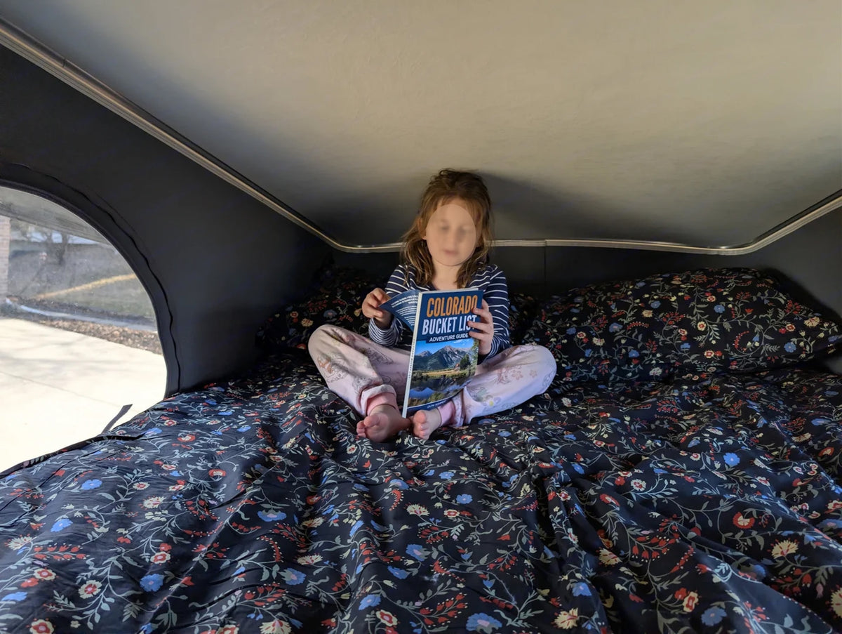Inside a cozy rv rental, a child reads "Colorado Bucket List" on a floral bed. Perfect for young adventurers. — photo 9