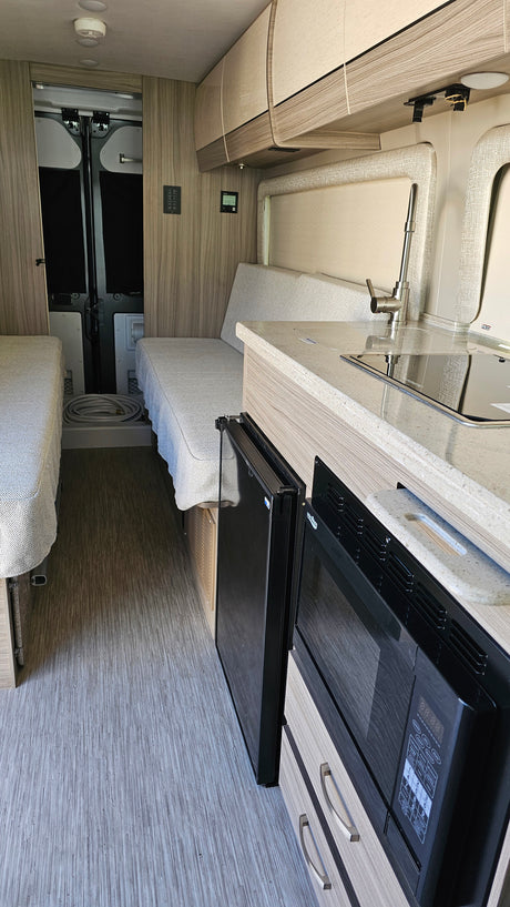 RV rental interior: cozy camper van with kitchen counter, sink, microwave, fridge, and convertible twin beds.