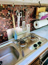 Compact RV rental kitchen with a stainless steel sink, two-burner stove, tiled backsplash, and hanging utensils.