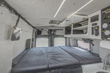 Spacious RV rental interior with a comfortable bed, overhead storage, control panel, and sink. Perfect for camper van adventures!