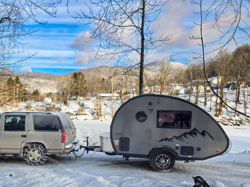  and a window view of the camper's wheel.|Winter RV rental: SUV with snow chains towing a T@B teardrop camper through a scenic — photo 4