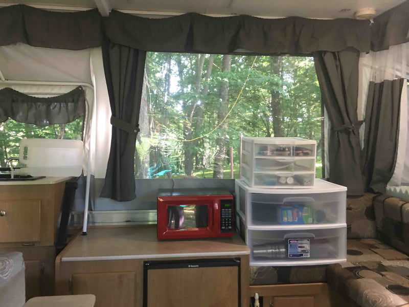 RV rental: interior with microwave, sink, storage, and large window to green trees. — photo 4