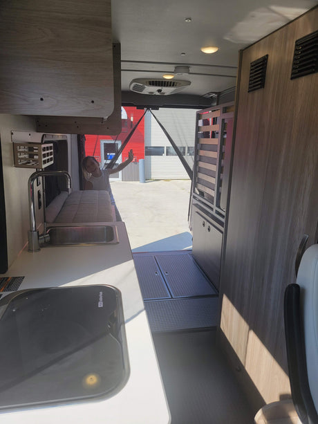 Enjoying an RV rental! A child waves from the open back of a modern camper van, featuring a compact kitchen and cozy interior.