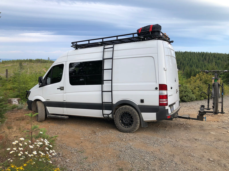 White rv rental adventure van with roof rack, ladder, and bike carrier parked on a scenic mountain trail. — photo 3