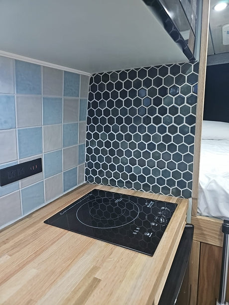 Compact RV rental kitchen features induction cooktop, wood counter, dual tiled backsplash, & outlets. Perfect for road trips.