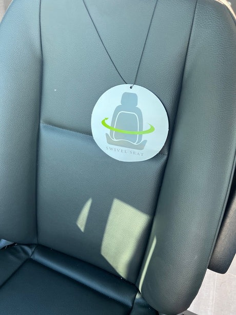 Close-up of a dark RV rental seat featuring a 'Swivel Seat' tag. The tag indicates a comfortable, rotating seat for convenience.