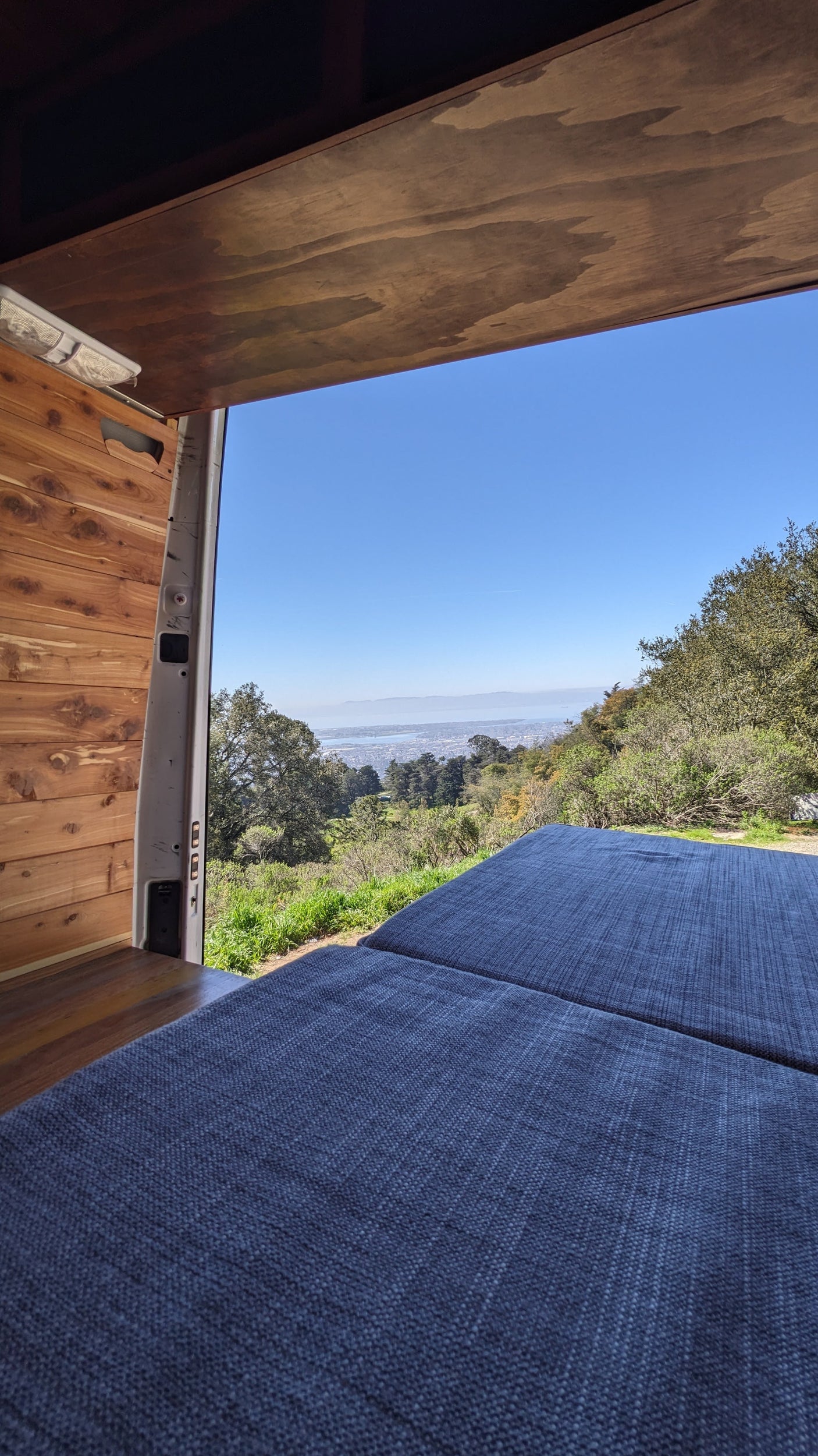 Interior of an RV rental van with blue cushions and open doors revealing a panoramic city and bay view from a scenic overlook.