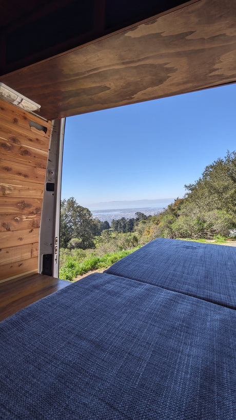 Interior of an RV rental van with blue cushions and open doors revealing a panoramic city and bay view from a scenic overlook.