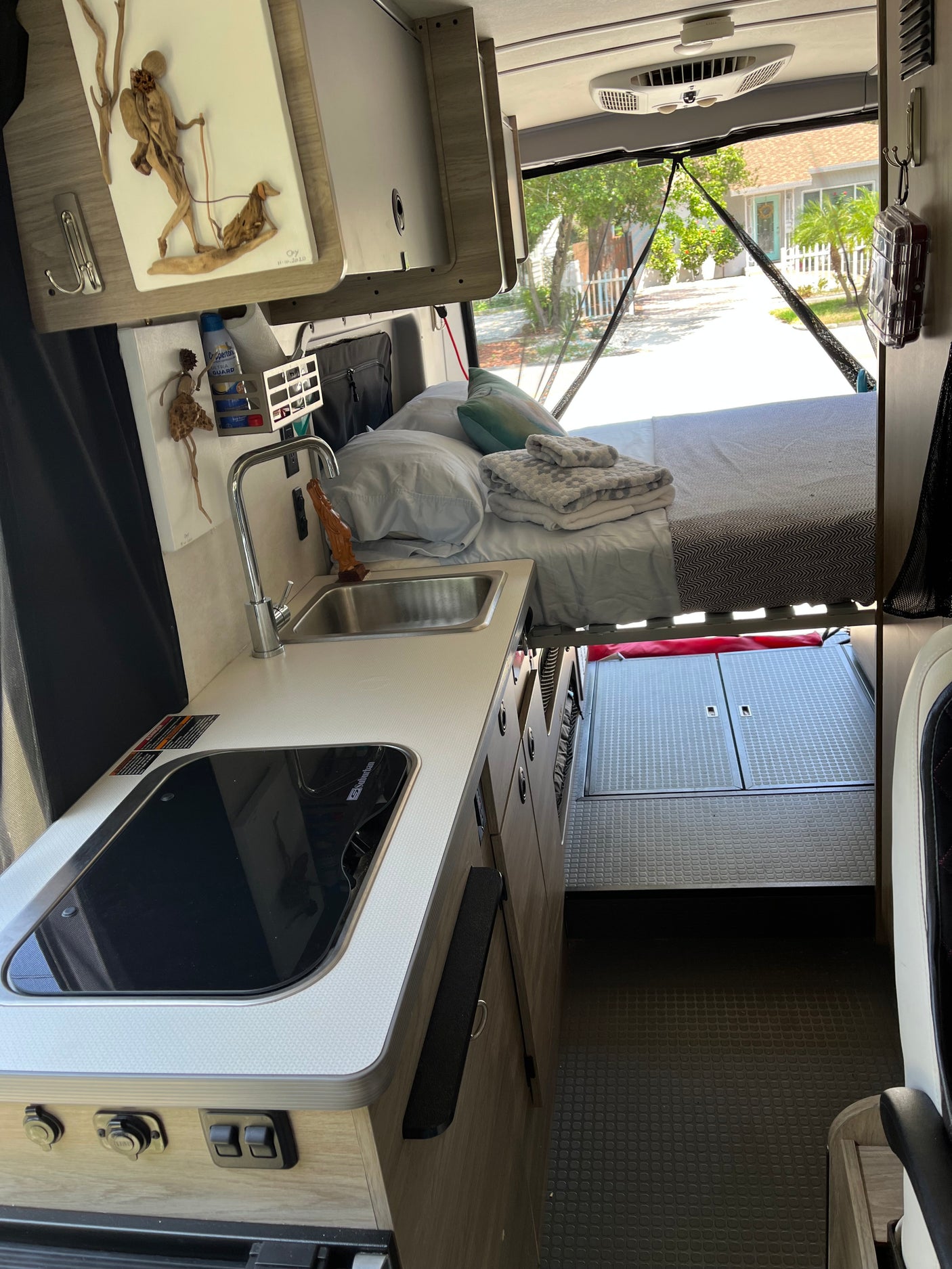 RV rental interior: compact kitchen (sink, stove), overhead storage, and a comfy bed with a view outside.