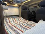 Cozy RV rental interior. Features a bed with a vibrant striped blanket, built-in entertainment, and front seats.