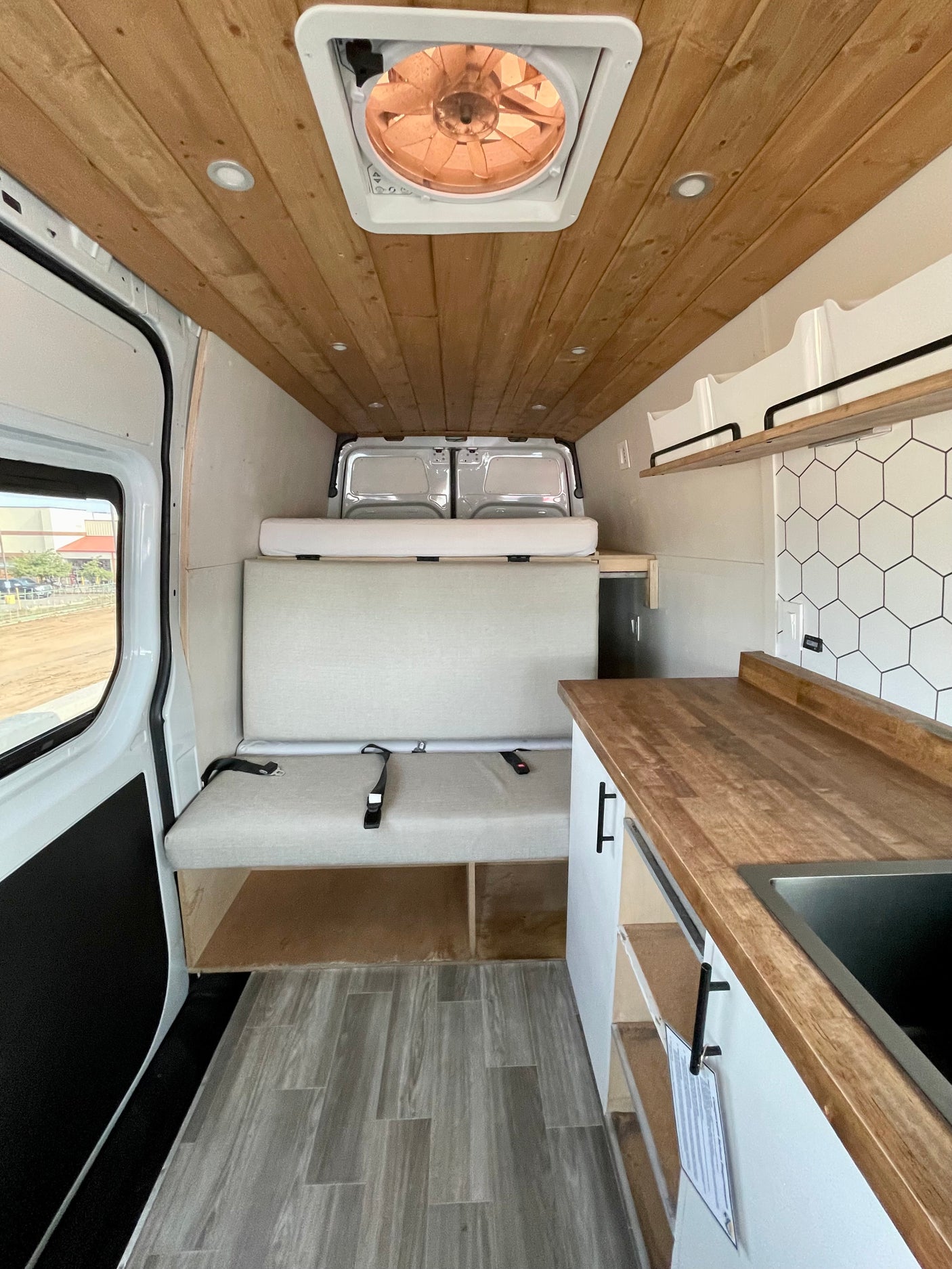 Spacious RV rental interior showcasing a wood-paneled ceiling, comfy bench with seatbelts, raised bed, and sleek kitchenette.