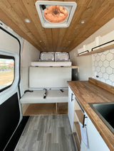 Spacious RV rental interior showcasing a wood-paneled ceiling, comfy bench with seatbelts, raised bed, and sleek kitchenette.
