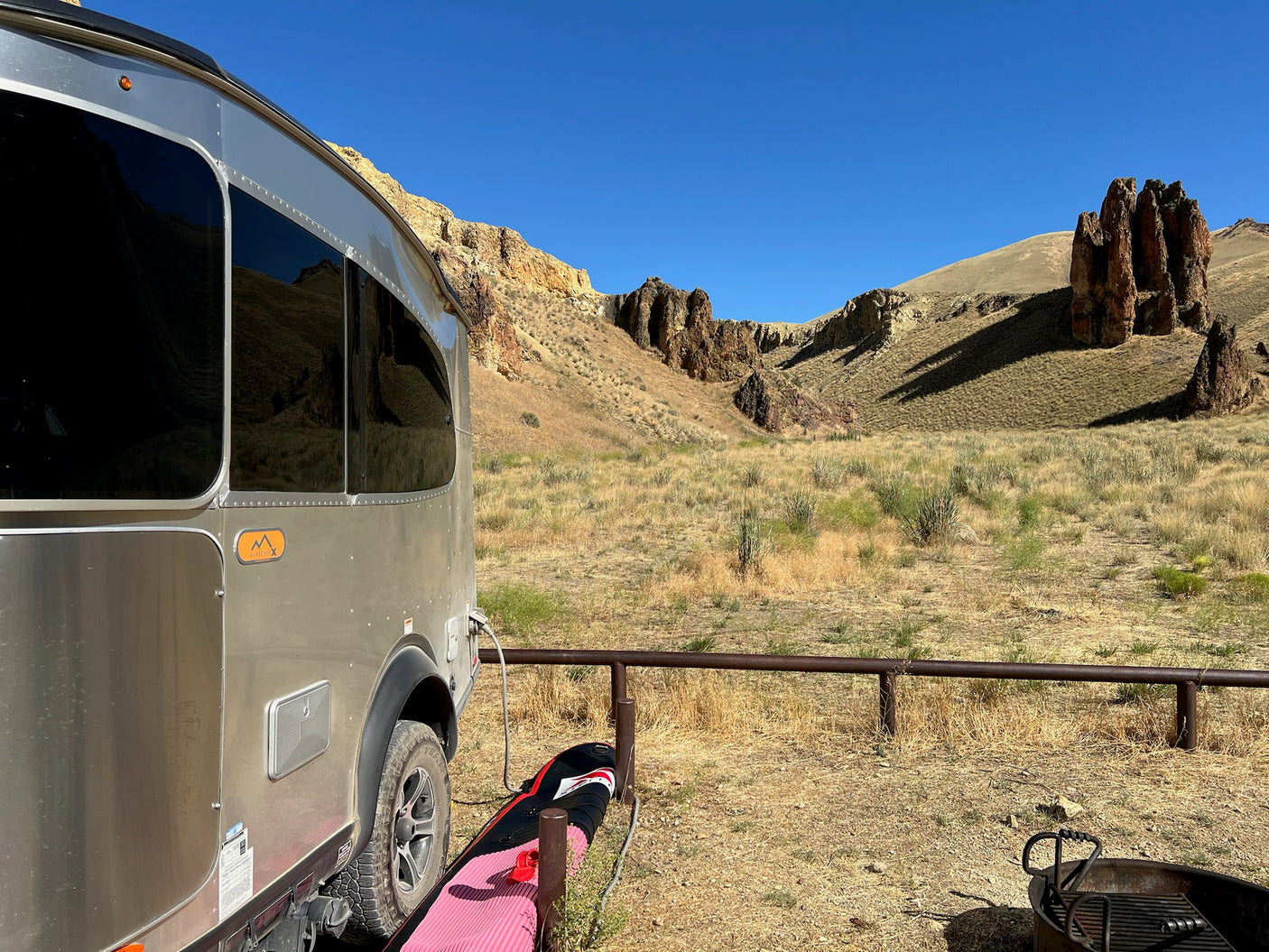 Silver RV rental parked in a stunning desert landscape with unique rock formations. Ready for adventure with paddleboard & fire pit.