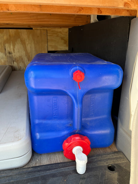 A blue Reliance water container with a white spigot inside an RV rental, providing essential water storage for your journey.