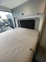 Cozy RV rental interior with a bed, overhead cabinets, and open rear doors, ready for travel.
