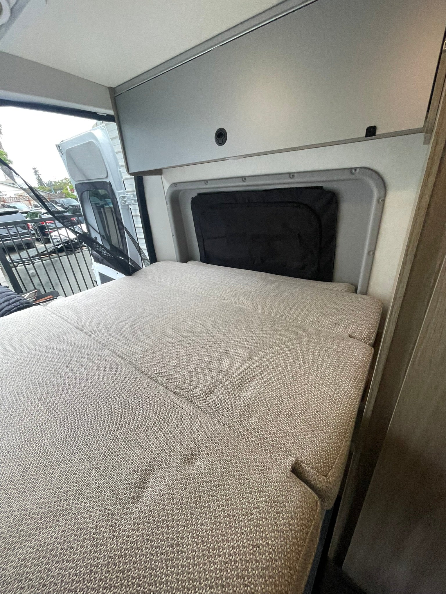 Cozy RV rental interior with a bed, overhead cabinets, and open rear doors, ready for travel.