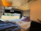 Cozy RV rental interior showcasing a comfortable bed, wooden ceiling, and a view out the rear window. Ideal for mobile travel.