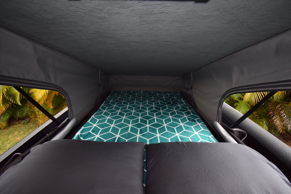 Cozy pop-top RV rental bed with geometric mattress & pillows, ready for adventure. Views of tropical foliage.