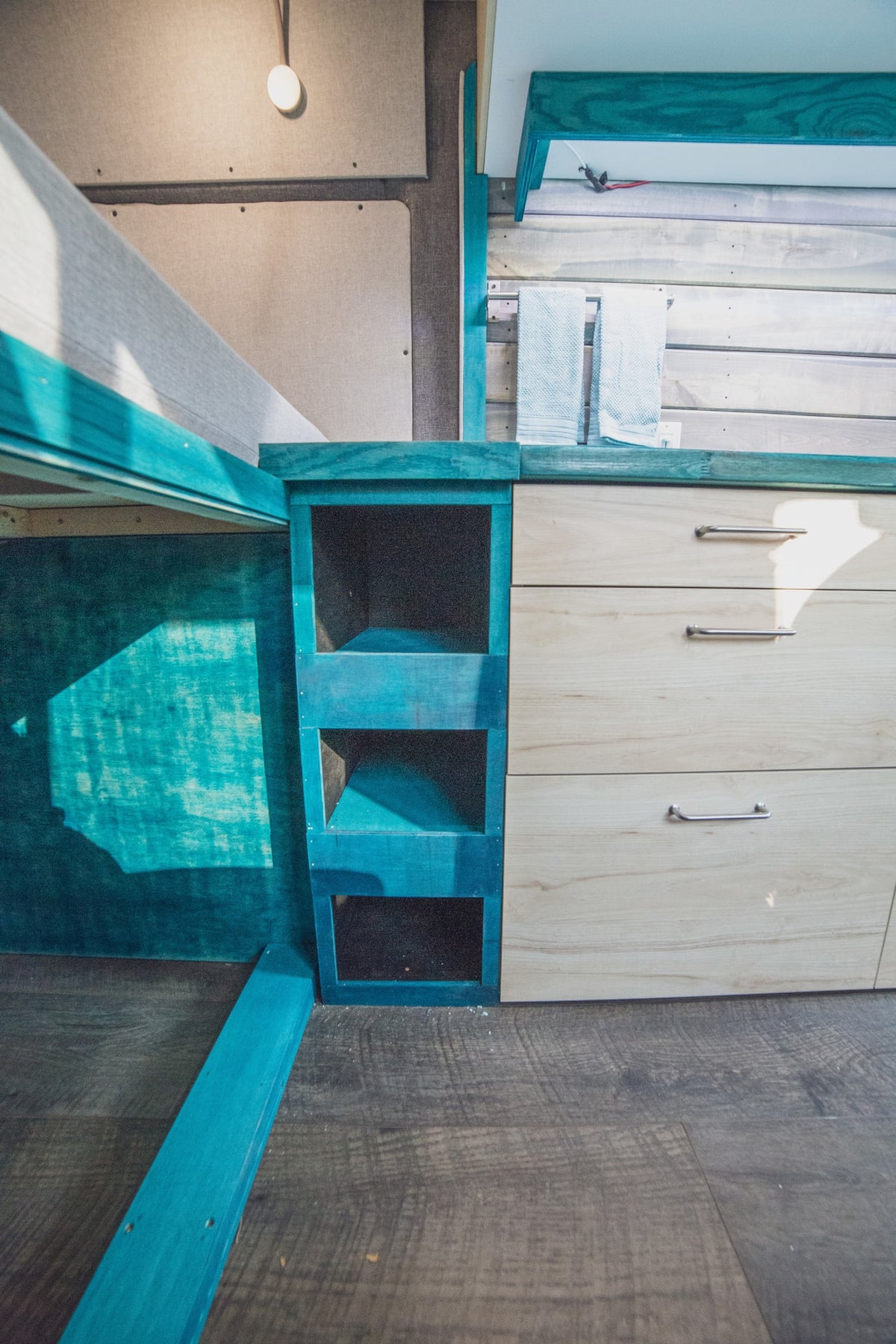 Compact RV rental interior featuring a turquoise bed frame, shelving, and wood drawers for smart storage. — photo 4
