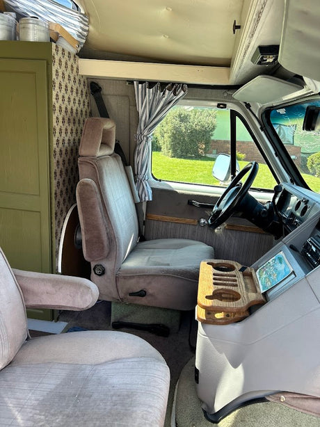Customized RV rental interior, featuring driver's area, custom seating, steering wheel, and front cabin with striped curtains.