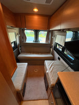 Comfortable RV rental interior with rear sofa/bed, side seating, kitchen counter, and overhead cabinets for a cozy mobile living space.