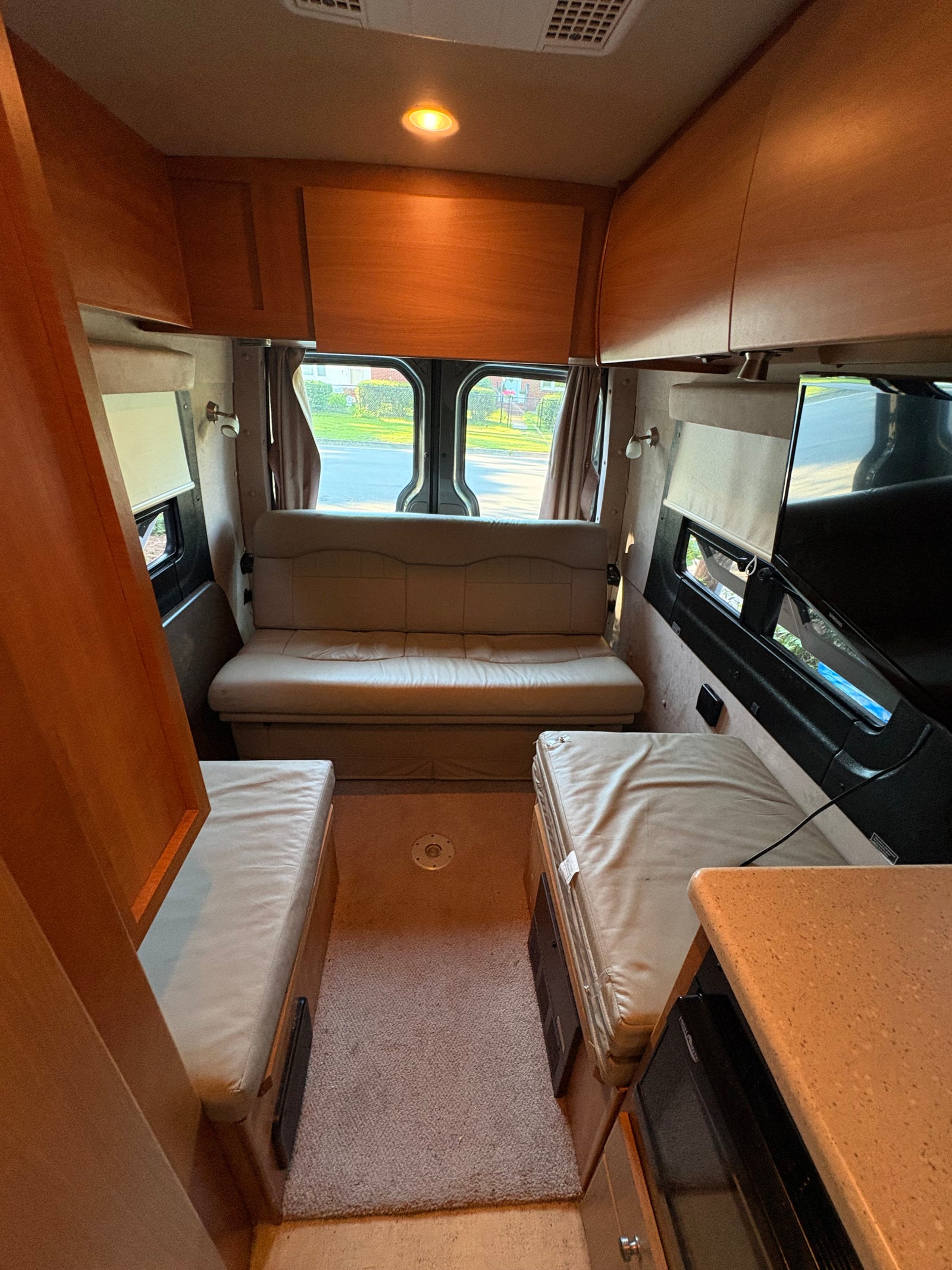 Comfortable RV rental interior with rear sofa/bed, side seating, kitchen counter, and overhead cabinets for a cozy mobile living space.