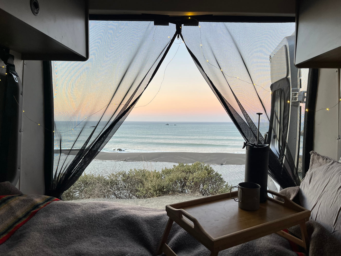 Inside an RV rental: a tranquil bedroom view of the ocean, beach, and sunset with string lights. — photo 5