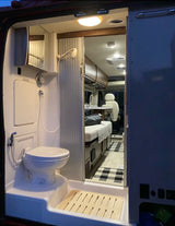 Compact RV rental interior featuring a wet bath with toilet & shower, plus a glimpse of the kitchen and sleeping area.