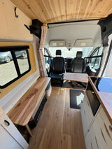 This RV rental camper van interior showcases a wooden ceiling, wood flooring, kitchen, bench seating, and front cabin access.