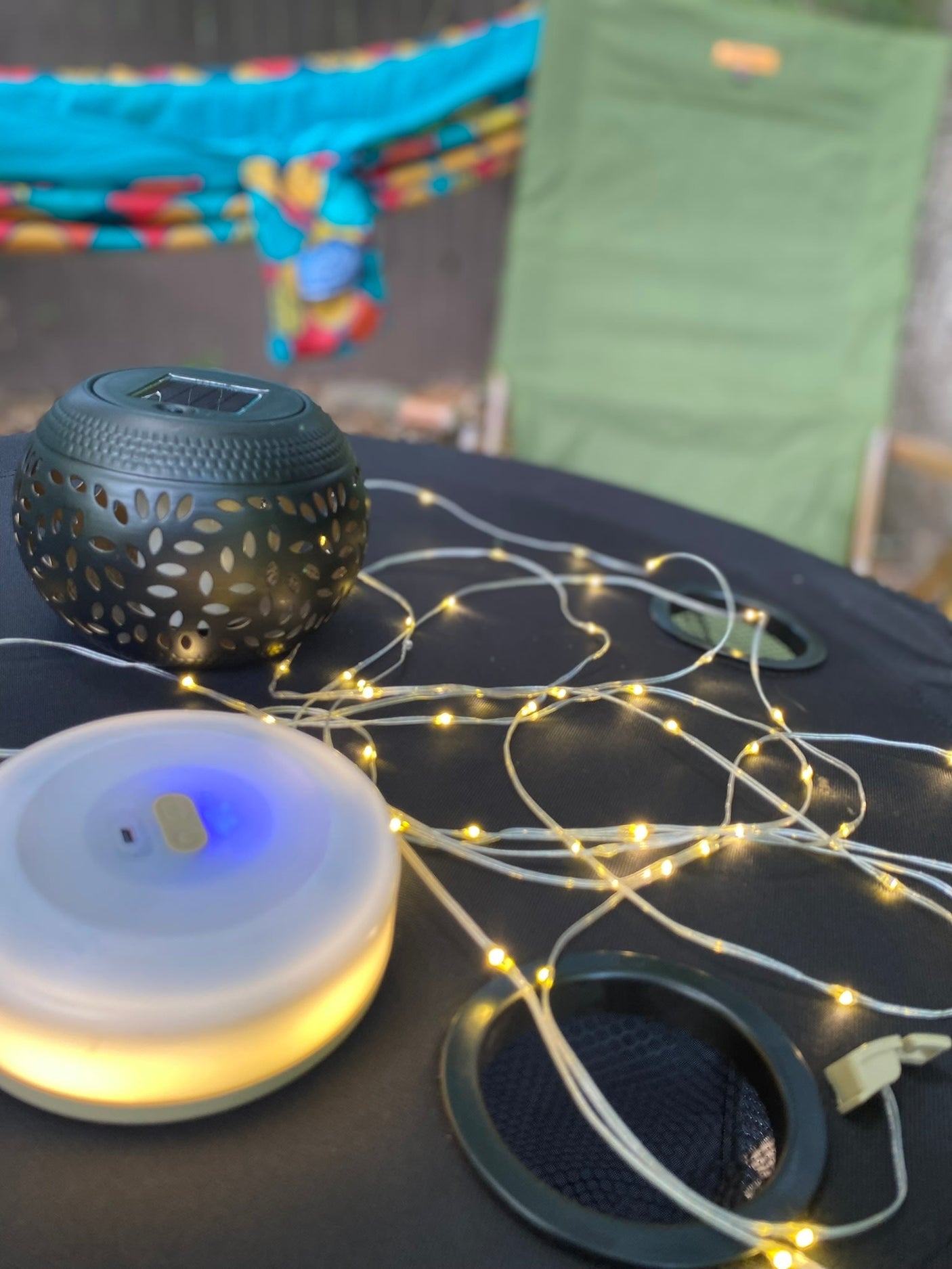 RV rental ambiance: Solar lantern, string lights, and portable light on table, by a hammock and camping chair.