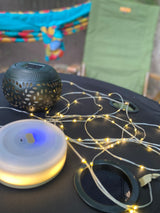 RV rental ambiance: Solar lantern, string lights, and portable light on table, by a hammock and camping chair.
