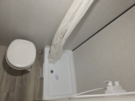 RV rental bathroom: overhead view of a compact toilet, shower, curtain, and soap dispenser.