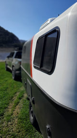 This compact RV rental, with its two-tone design & red stripe, is parked on green grass, ready for adventure in scenic outdoors.
