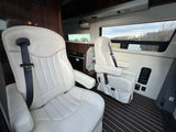 RV rental's cozy interior: two cream captain's chairs, a compact kitchen, and large scenic windows visible.
