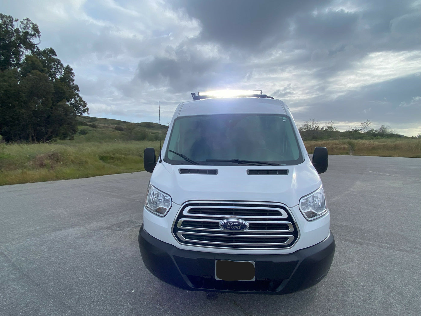 White Ford Transit van with rooftop light bar, ideal for your next RV rental adventure, parked under a cloudy sky. — photo 13